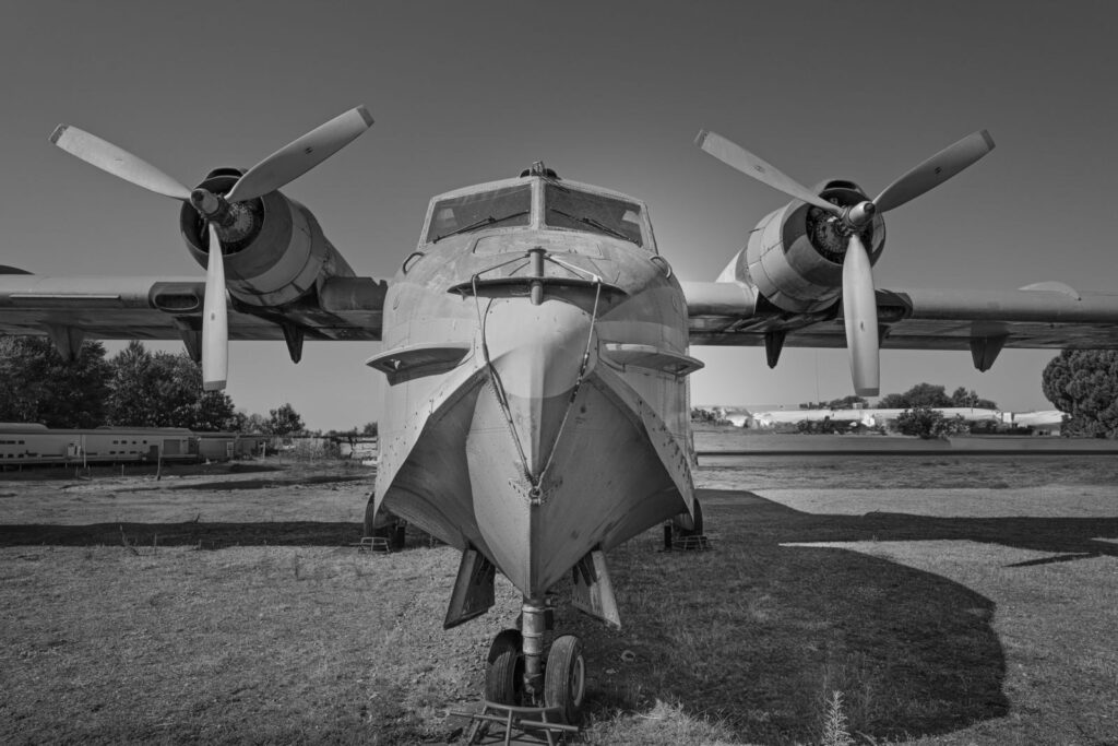Grayscale image of a vintage aircraft with propellers in a field, evoking historical aviation era.