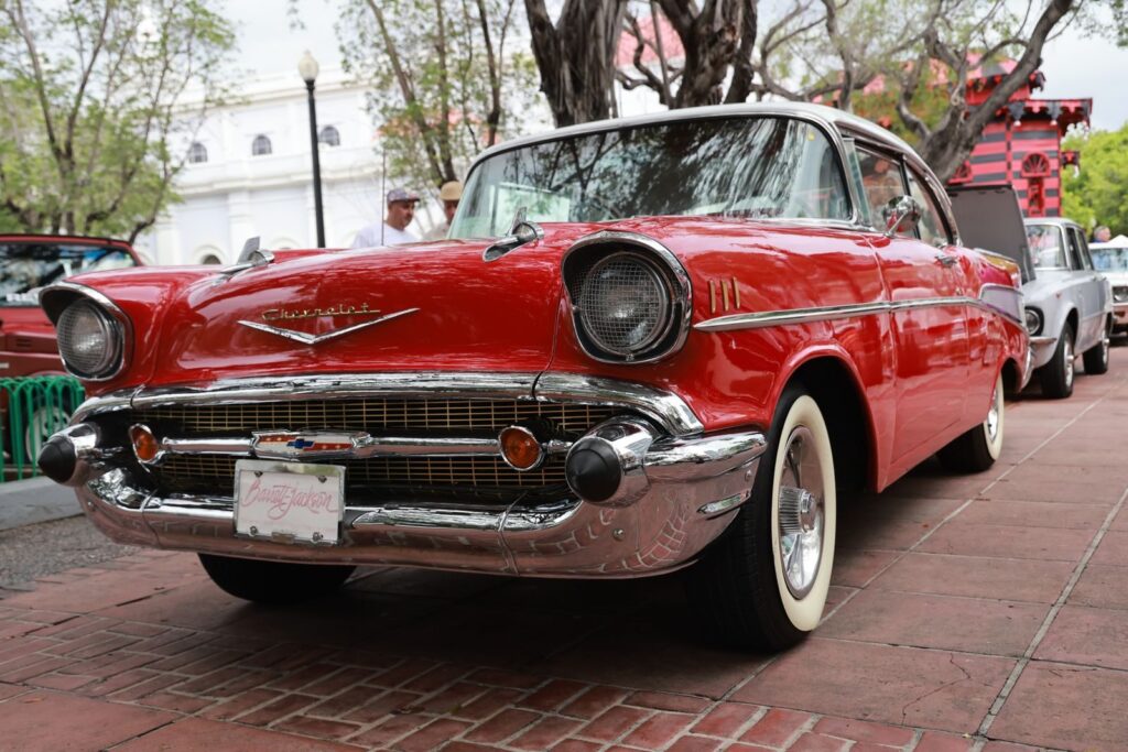 A classic red 1957 Chevrolet on display outdoors with people admiring it.