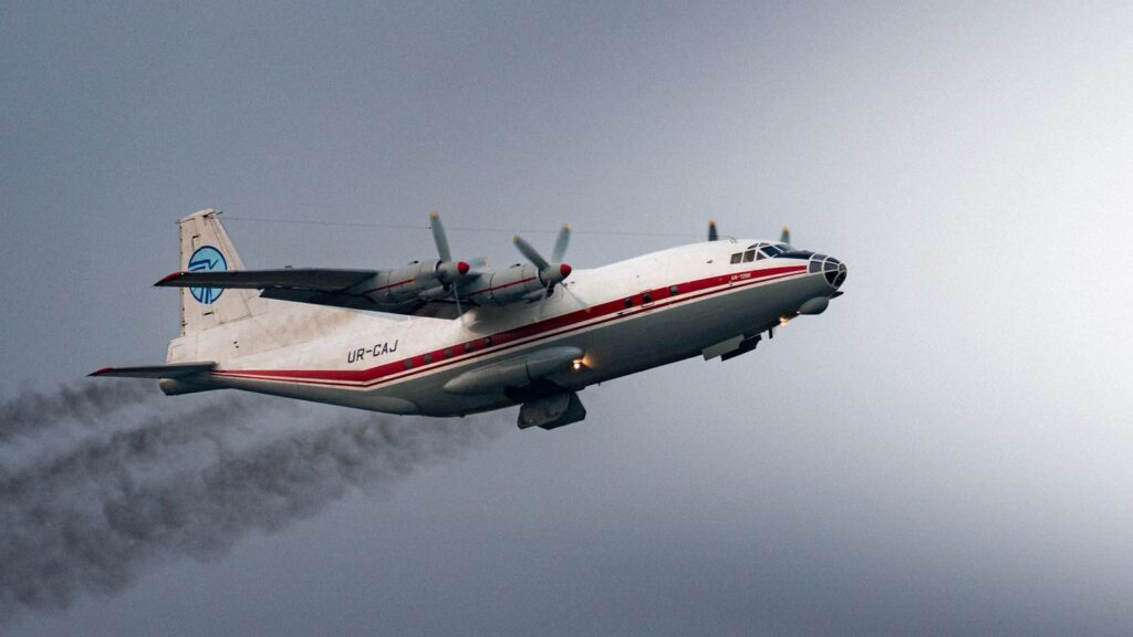 An airplane with identification UR-CAJ emitting black smoke under a cloudy sky in Sepang, Malaysia.