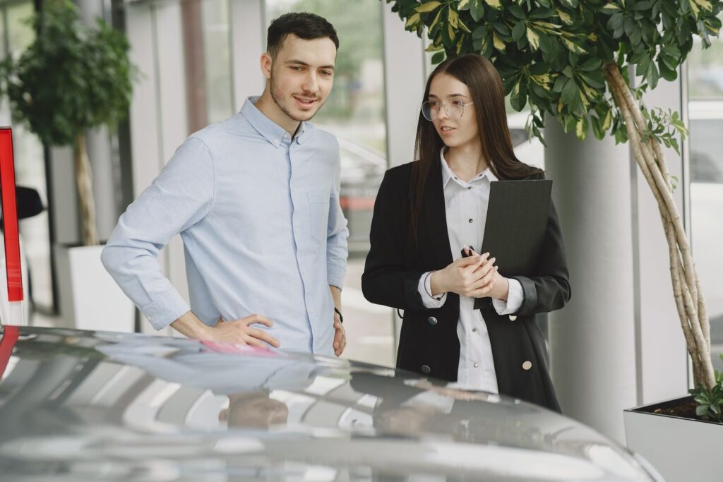 Two professionals discussing business in a modern car showroom with plants around.