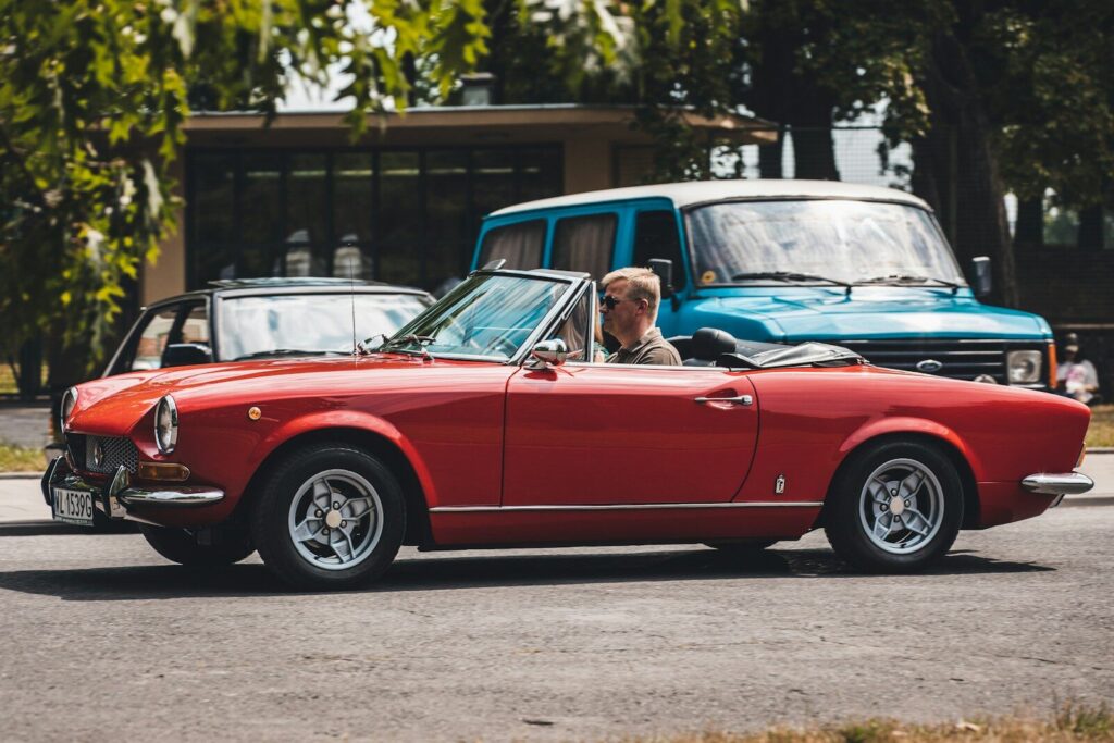 a man driving a red convertible car down a street
