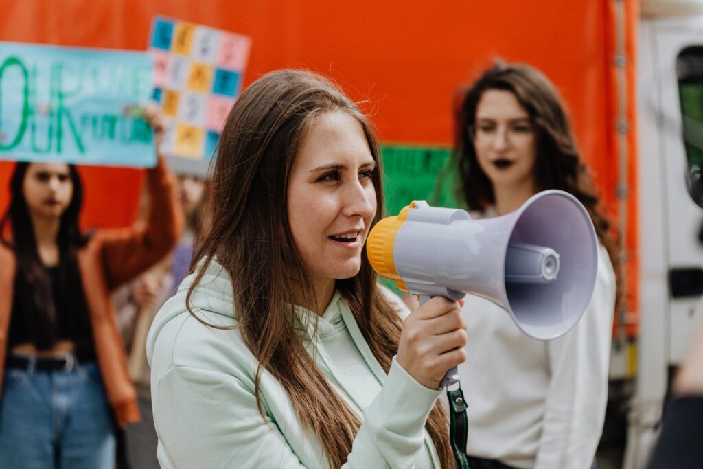 Close-up of women at a protest holding a megaphone and placards in a lively demonstration.