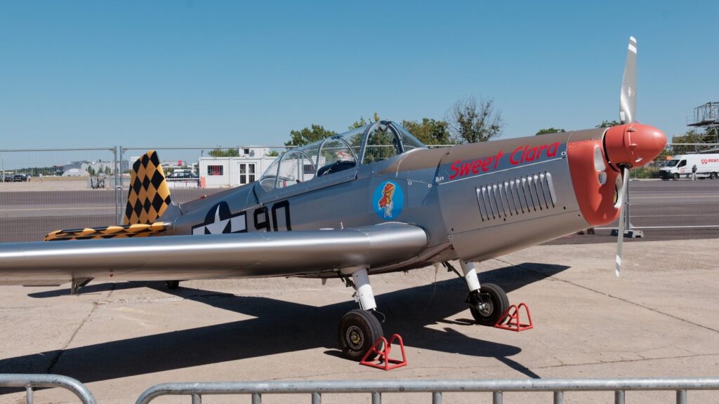 Silver vintage airplane with red nose and tail.