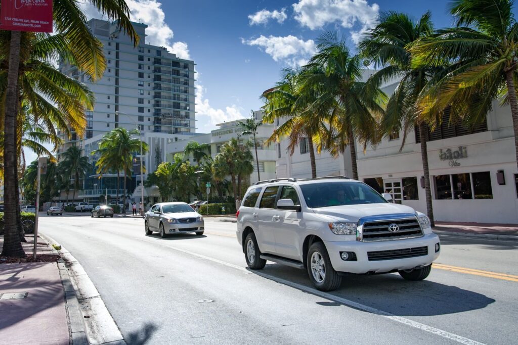 A vibrant city street lined with palm trees and modern buildings under a bright sky.