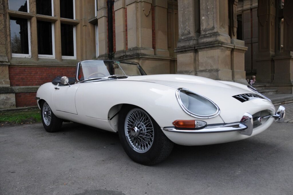 Classic white Jaguar E-Type parked outside a historic building, showcasing timeless luxury and style.