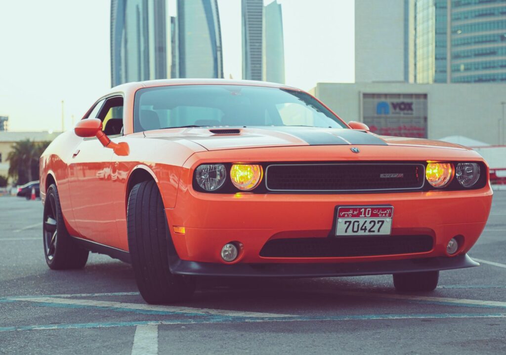 Vibrant orange Dodge Challenger SRT on display in a Dubai parking lot at sunset.