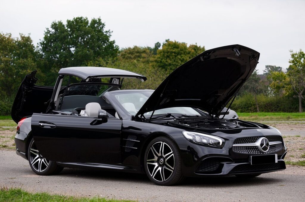 A modern black Mercedes-Benz SL400 with open hood and roof, parked in a serene park setting.