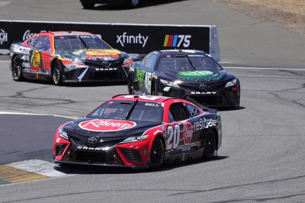 Dynamic stock car race with colorful vehicles speeding on a sunlit track at a major event.