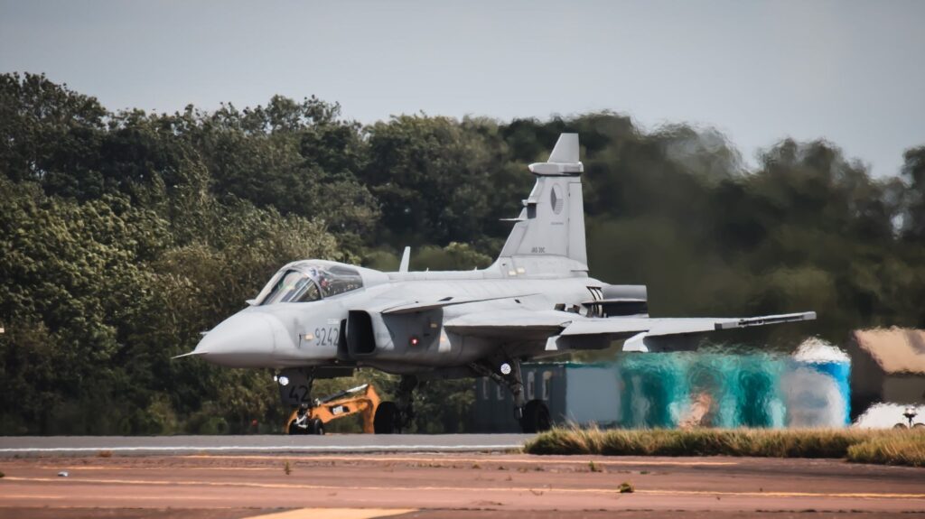 Close-up of a military jet aircraft at an airport runway in England, surrounded by greenery.