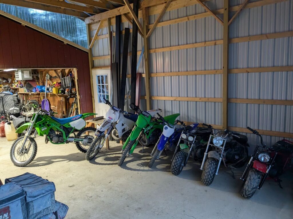 Parked dirt bikes and motorcycles inside a spacious workshop garage.