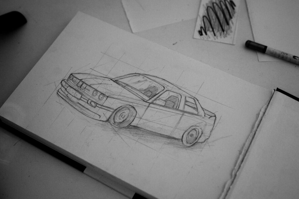 Detailed pencil sketch of a classic car on a sketchpad with art supplies nearby.