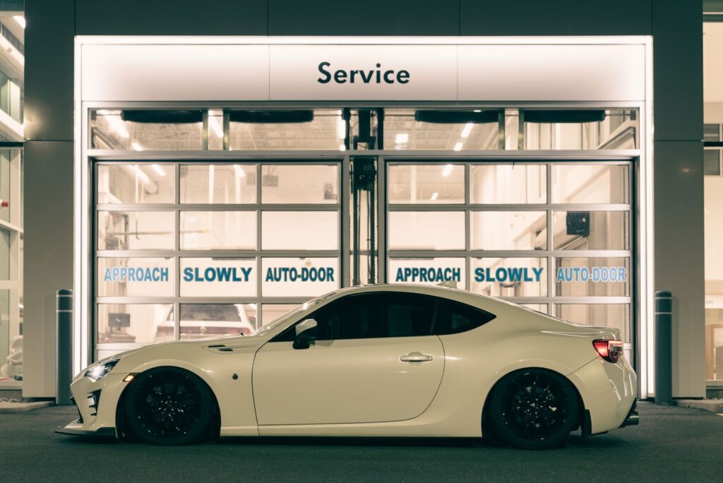 A stylish white sports car parked outside a service center at night, under glowing lights.
