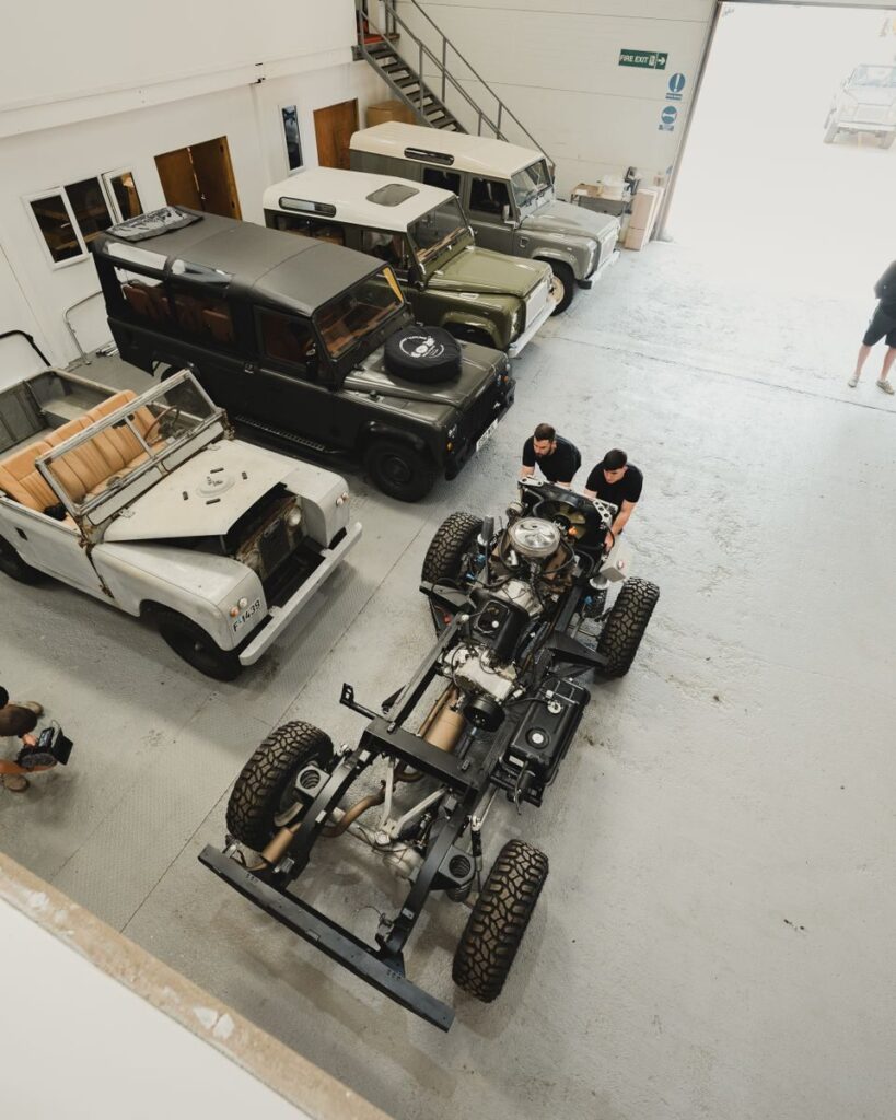 A bustling auto workshop with mechanics restoring vintage Land Rovers viewed from above.