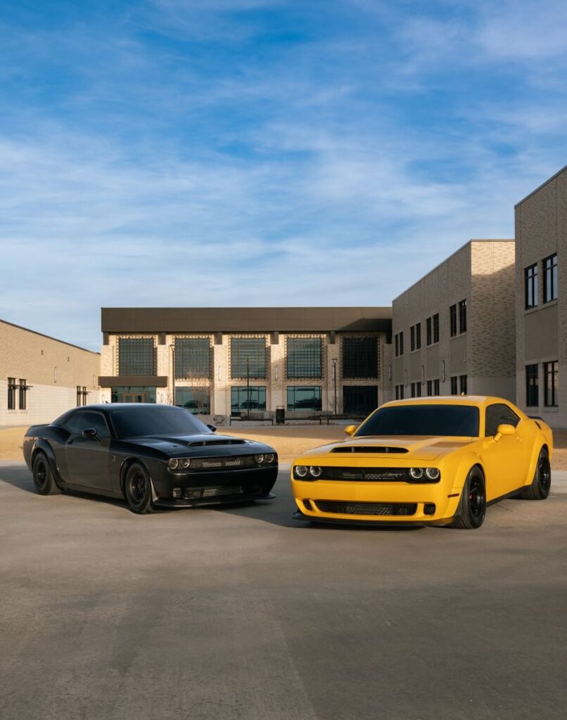 Black and yellow Dodge Challengers parked in front of modern buildings on a sunny day.