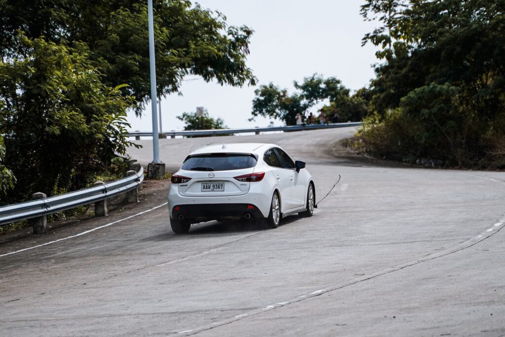 A white car navigates a curving mountain road amidst lush greenery in Mangatarem, Ilocos Region, Philippines.
