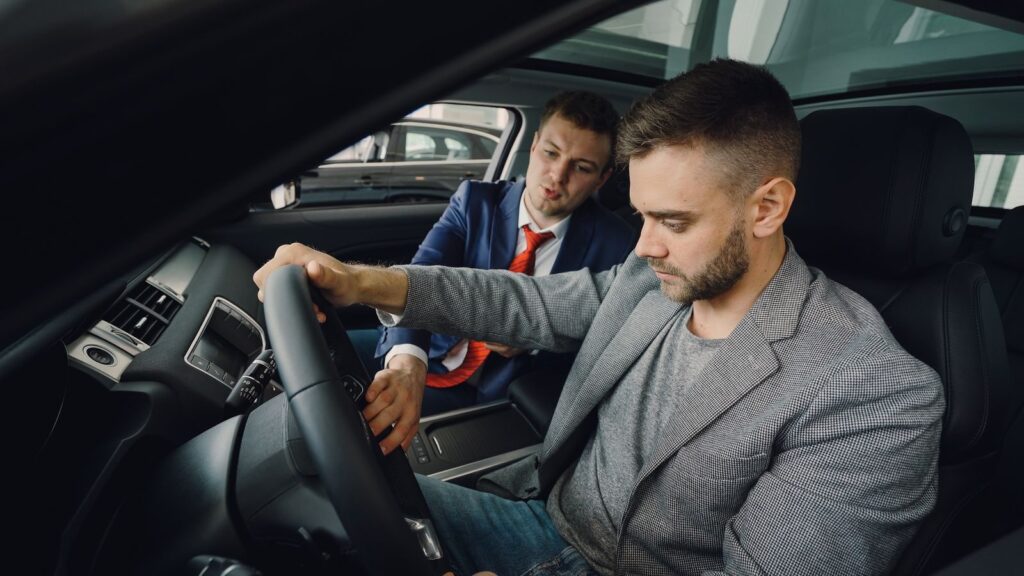 Salesman demonstrating car features to potential buyer inside vehicle showroom.