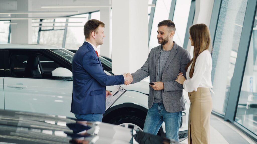 A couple completes a transaction with a salesman at a modern car dealership.