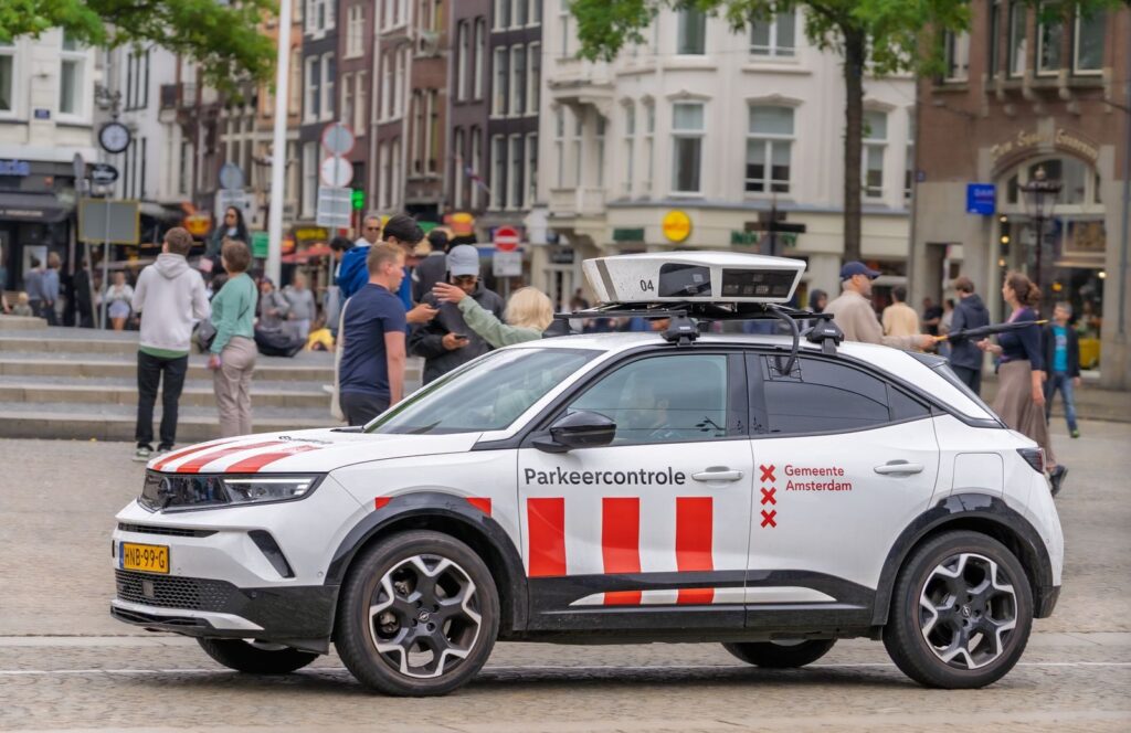 Parking control vehicle in Amsterdam city square, capturing urban life and crowd interaction.