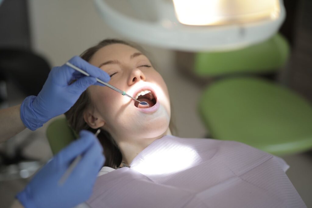 From above view of crop unrecognizable dentist in latex gloves using medical instruments while examining teeth of patient during work in modern dental room
