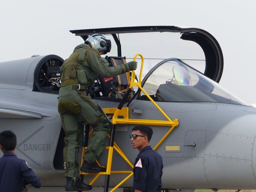 Military pilot preparing for flight, climbing into fighter jet cockpit with support crew nearby.