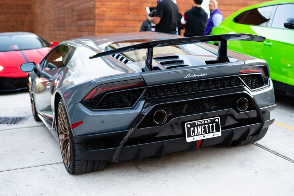 Rear view of a luxury Lamborghini sports car with custom Texas license plate at an outdoor car event.