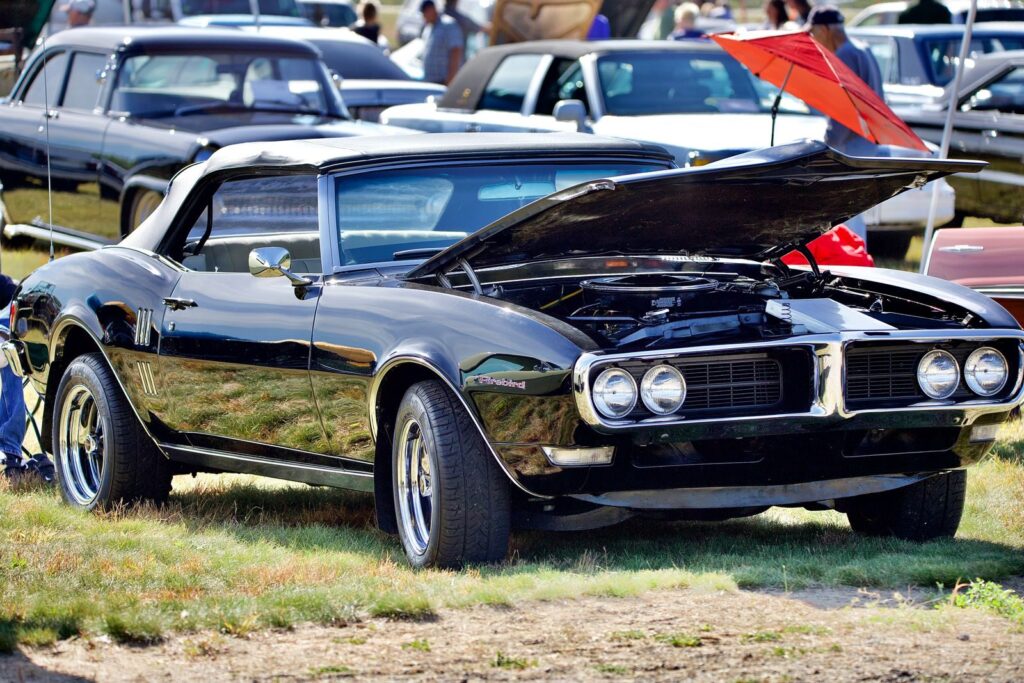 Stunning black Pontiac Firebird muscle car with hood open, displayed at an outdoor car show.