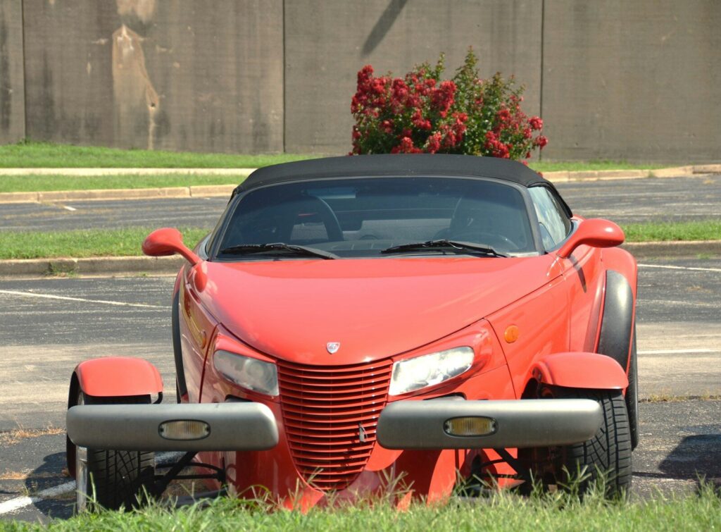 A red Plymouth Prowler convertible parked on an asphalt lot with red flowers