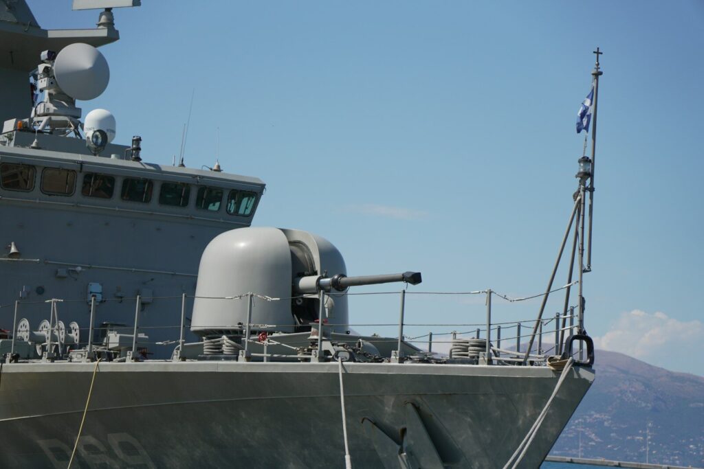 Naval warship's bow with a large gun and flying flag.