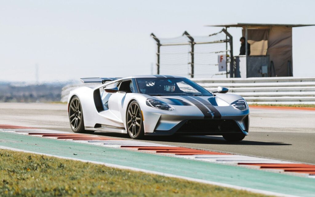 A silver sports car driving on a paved racetrack with a guardrail