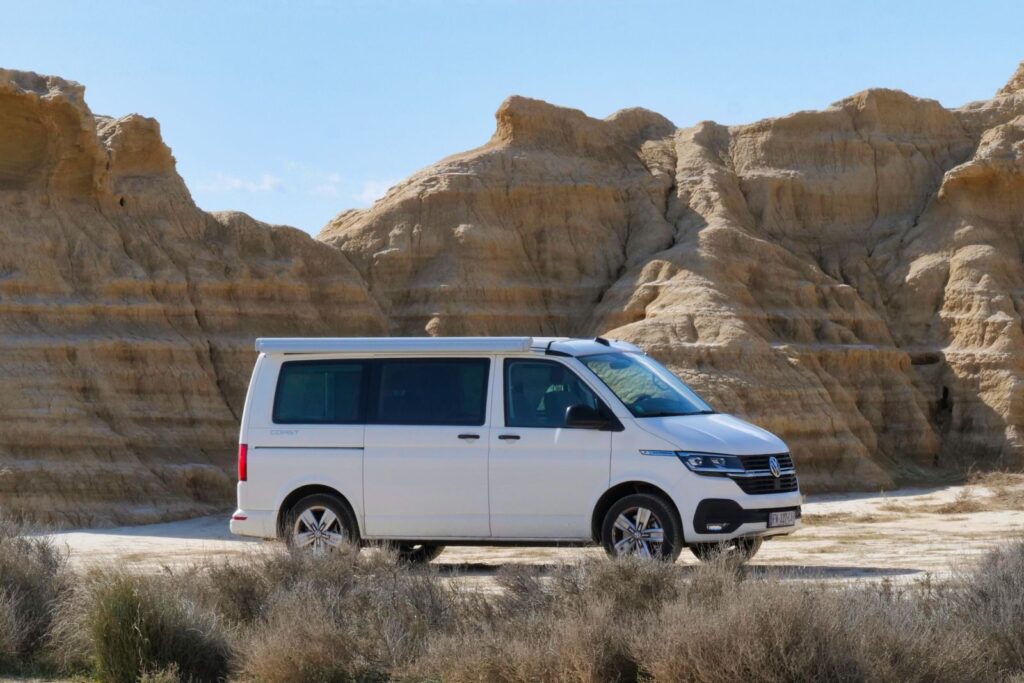 White camper van parked in striking desert landscape with rock formations under clear blue sky.