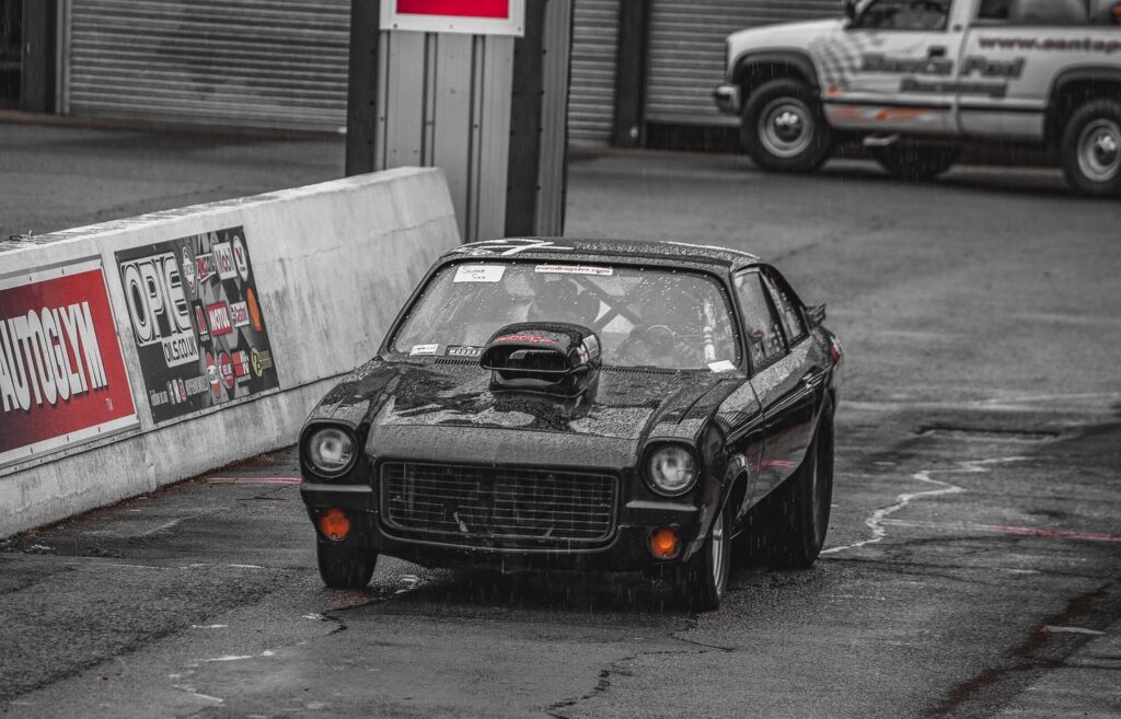 A black classic car takes on a wet racing track during a motorsport event, showcasing power and speed.