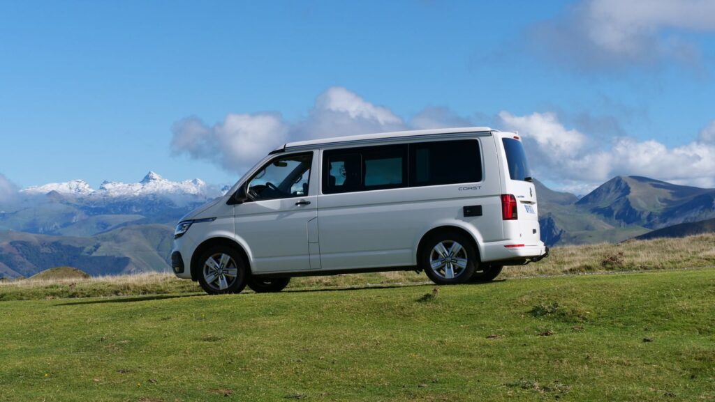 White van parked on a lush green field with stunning mountain background under blue skies.