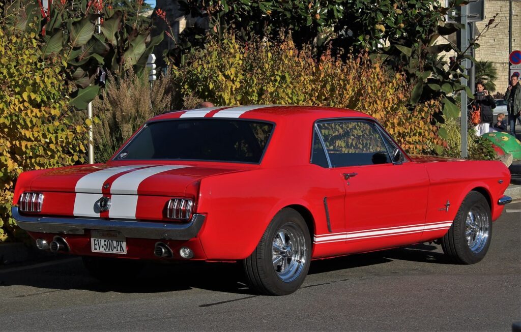 Classic red Ford Mustang parked outdoors amidst foliage.