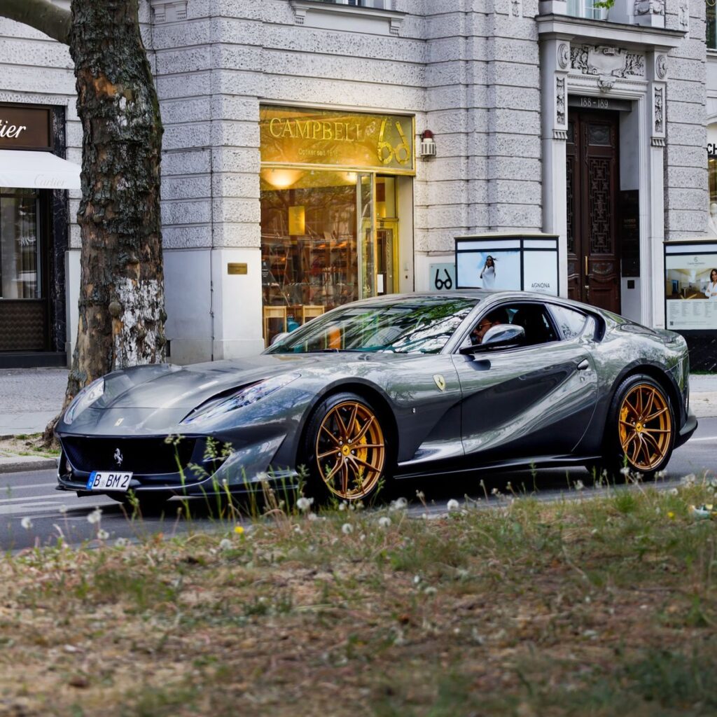 A sleek gray sports car parked in an urban setting with stylish architecture in the background.
