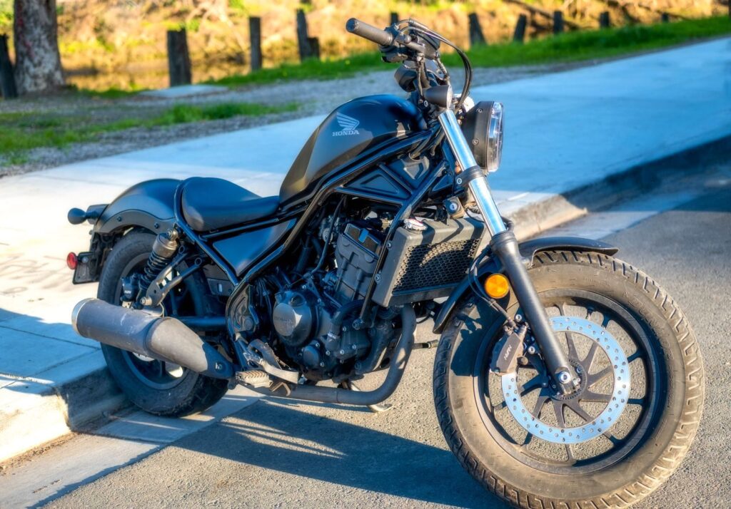 A stylish black motorcycle parked on a sunny street, showcasing details of its engine and tire.
