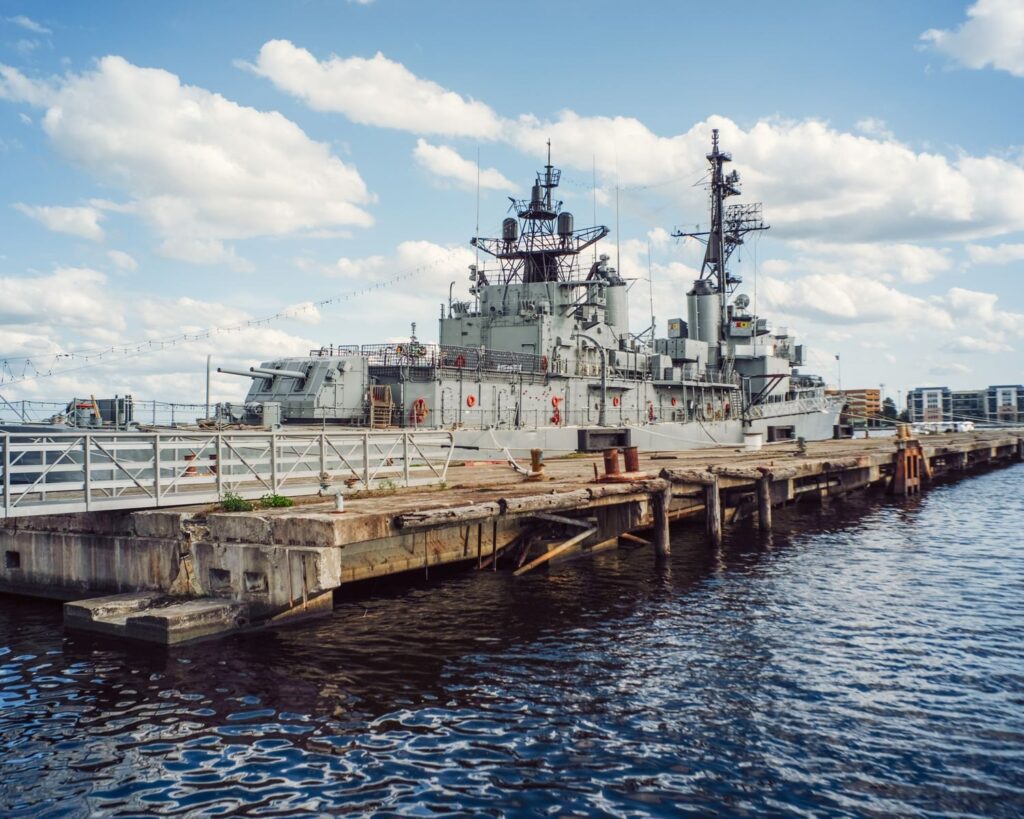 A decommissioned warship anchored at a naval museum pier under a clear sky.