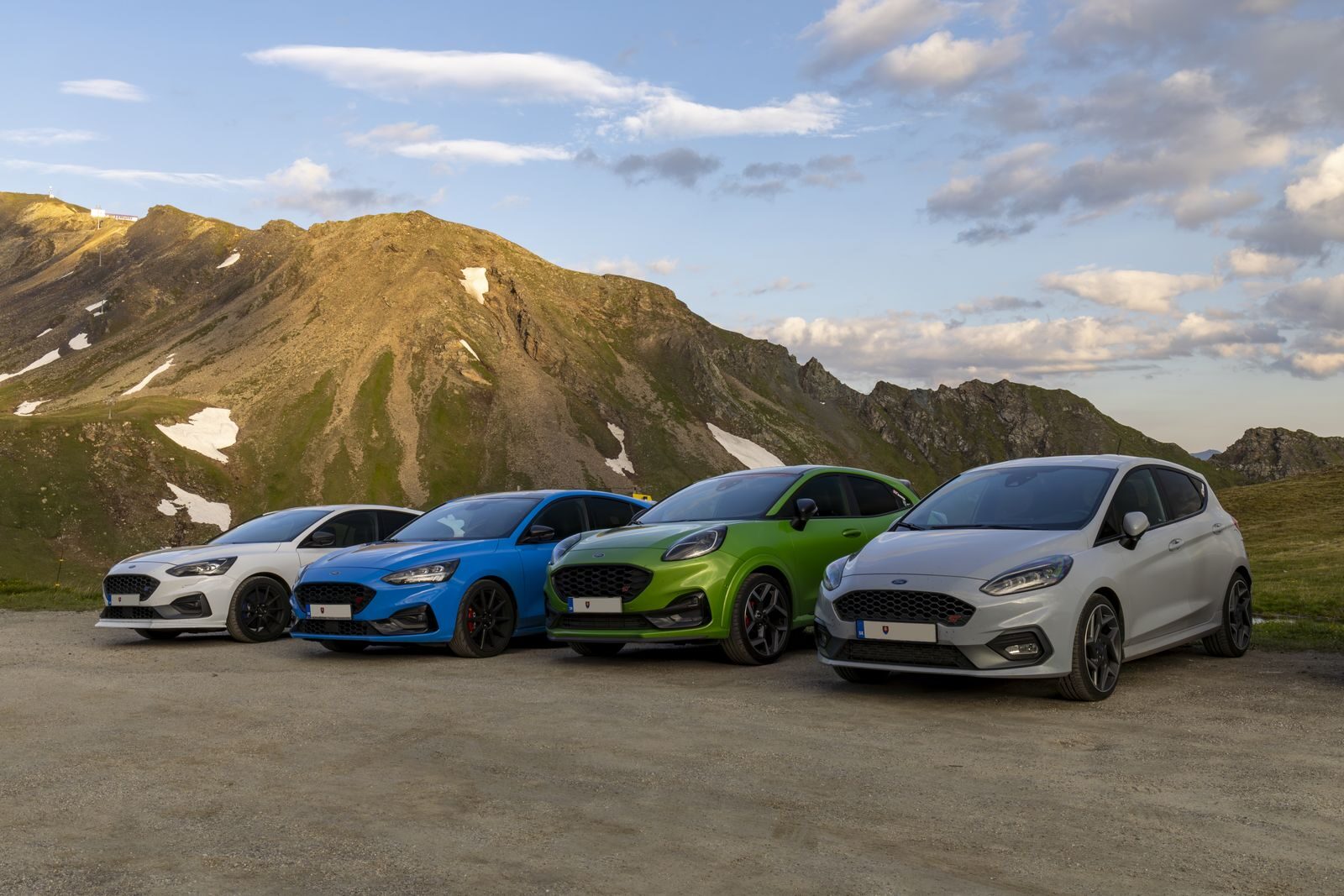 A lineup of vibrant modern cars parked against a stunning mountain backdrop.