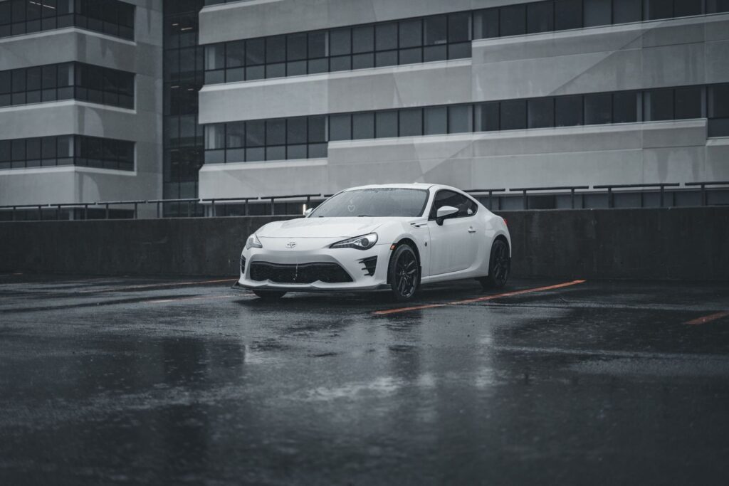 A sleek white sports car parked in a rainy cityscape, showcasing modern urban architecture.