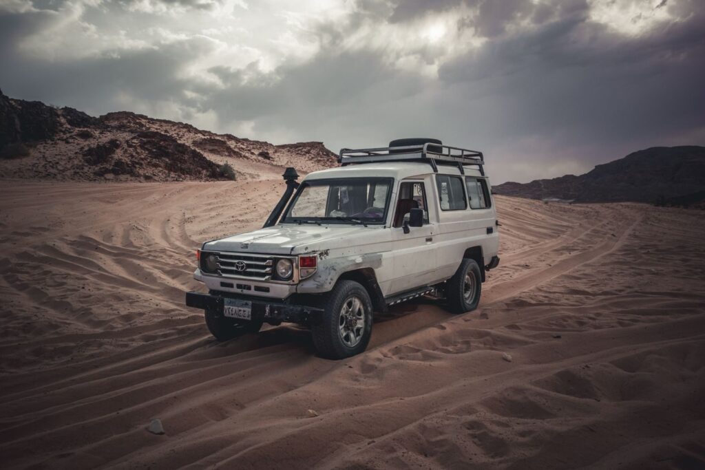 Toyota SUV drives through expansive desert sands under a cloudy sky, showcasing adventure.