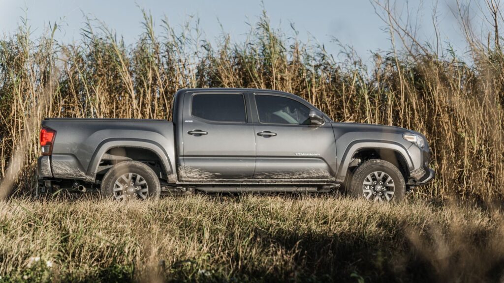 Toyota Tacoma parked on a rural dirt road with tall grasses in the background.