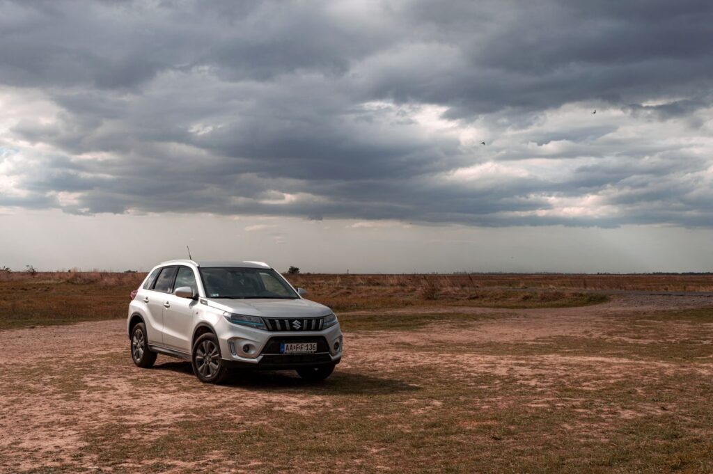 A silver SUV parked on a rural dirt path with dramatic cloud formations in the sky.