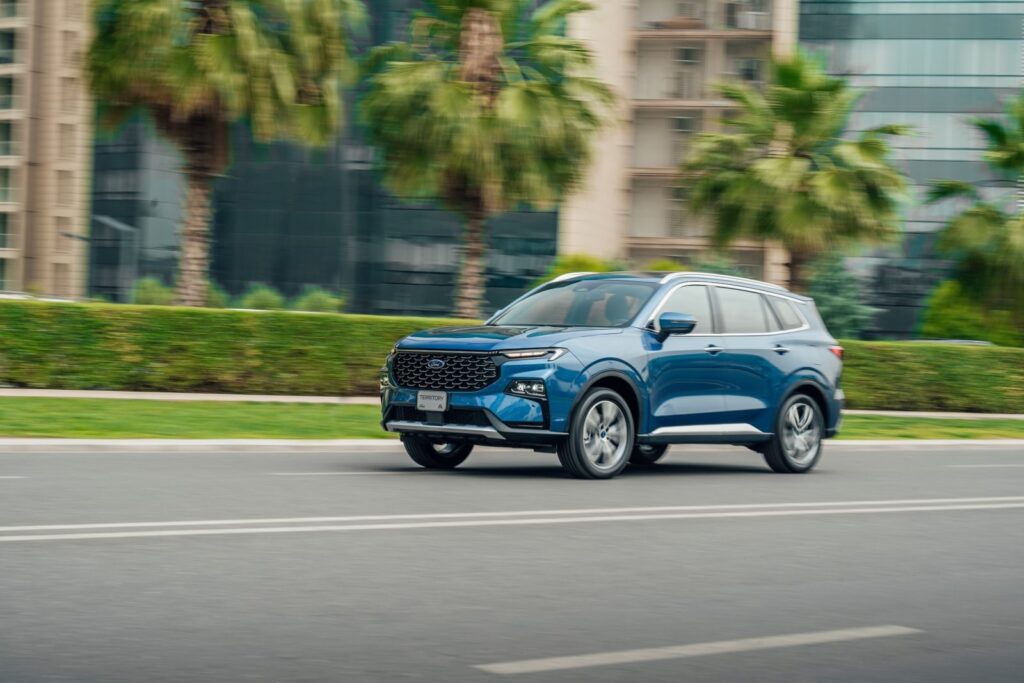 Blue SUV driving on a modern street in Erbil, Iraq with palm trees and buildings.