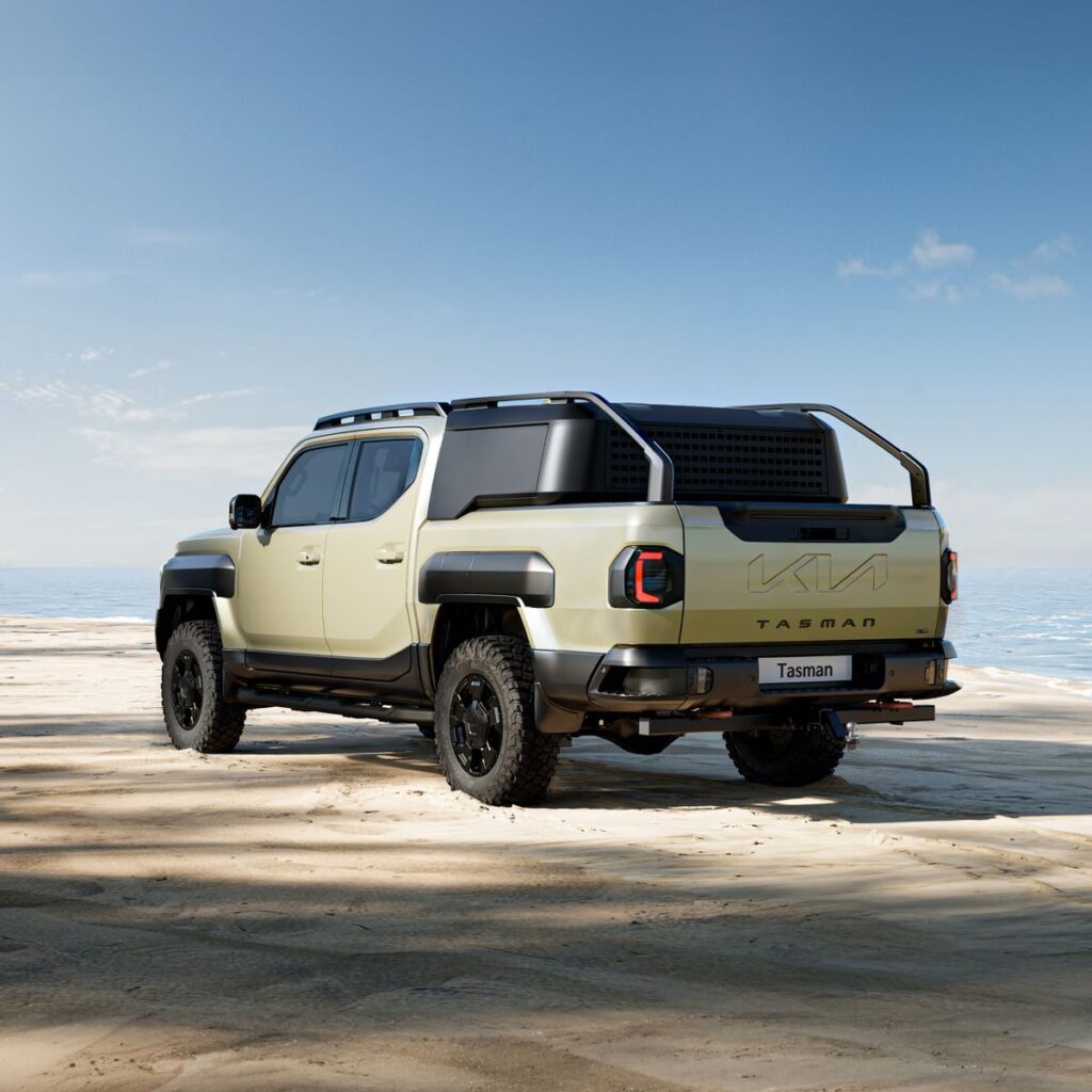 A sleek Kia Tasman pickup truck parked on a sunny beach with ocean views.