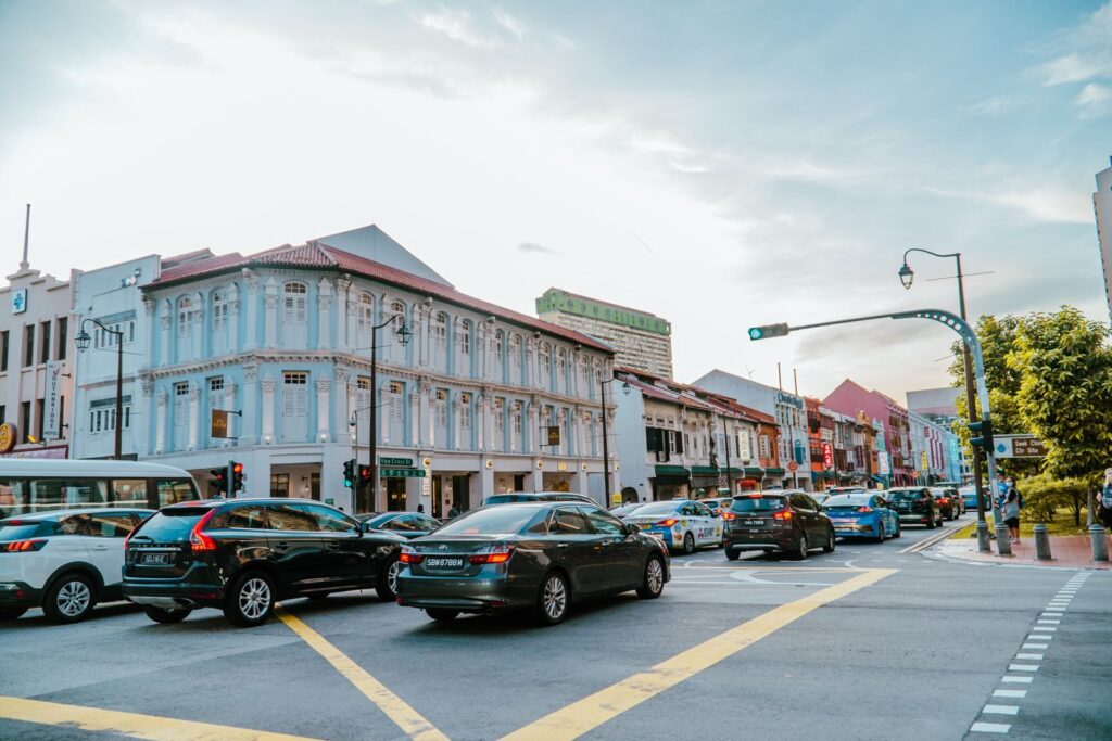 Busy street intersection with traffic and historic shophouses in downtown Singapore during the day.