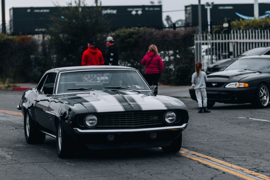 A vintage Chevrolet Camaro parked on a Los Angeles street with people in the background.