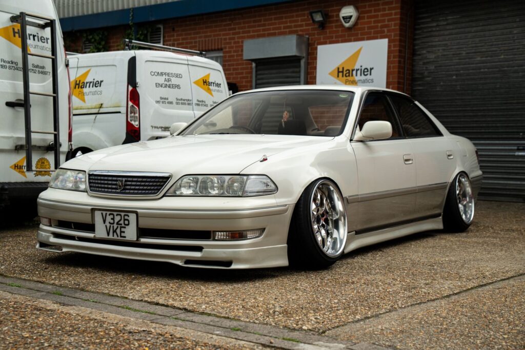 A stylish, modified white sedan parked outside a garage in Southampton, England.