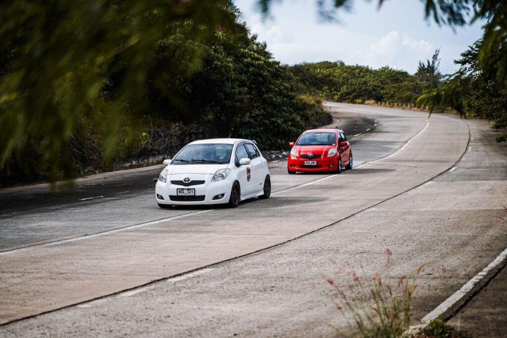 White and red cars navigate a scenic curved road in Mangatarem, Philippines.