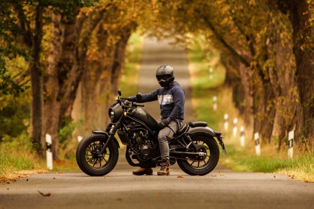 Motorcyclist sits on a bike on a picturesque country road flanked by trees.