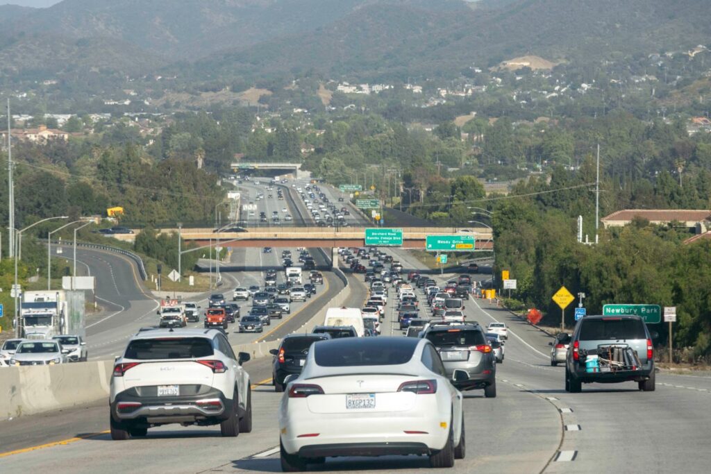 Heavy traffic on a Los Angeles highway with visible road signs and cars under a clear sky.