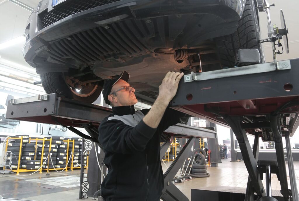 Mechanic inspecting car on lift in an automotive garage, focusing on vehicle repair and maintenance.